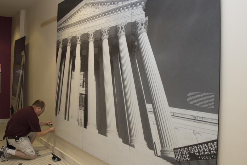 Nicholas Traub, graphic designer for Traub Design Associates, mounts an image of the Supreme Court Building, which is located near the Chadron State College Justice Studies Department's offices in Old Admin. (Photo by Justin Haag)